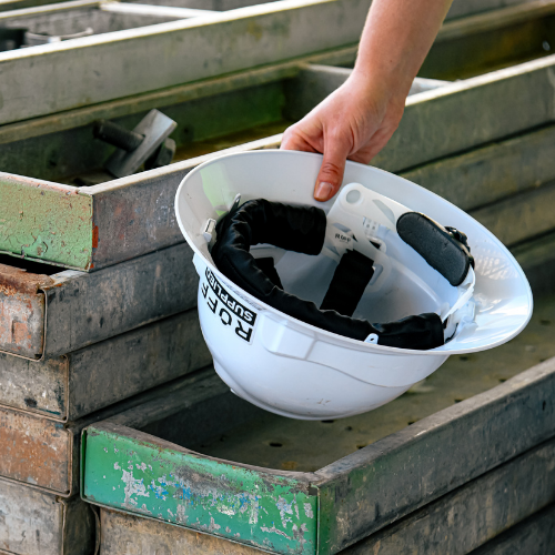 Worker holding a hard hat with a fitted Ruff Supplied sweatband in their hand and placing on a stack of timber